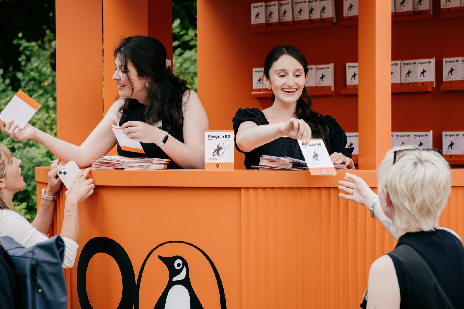 Hosts handing out material from a bright orange Penguin-branded kiosk