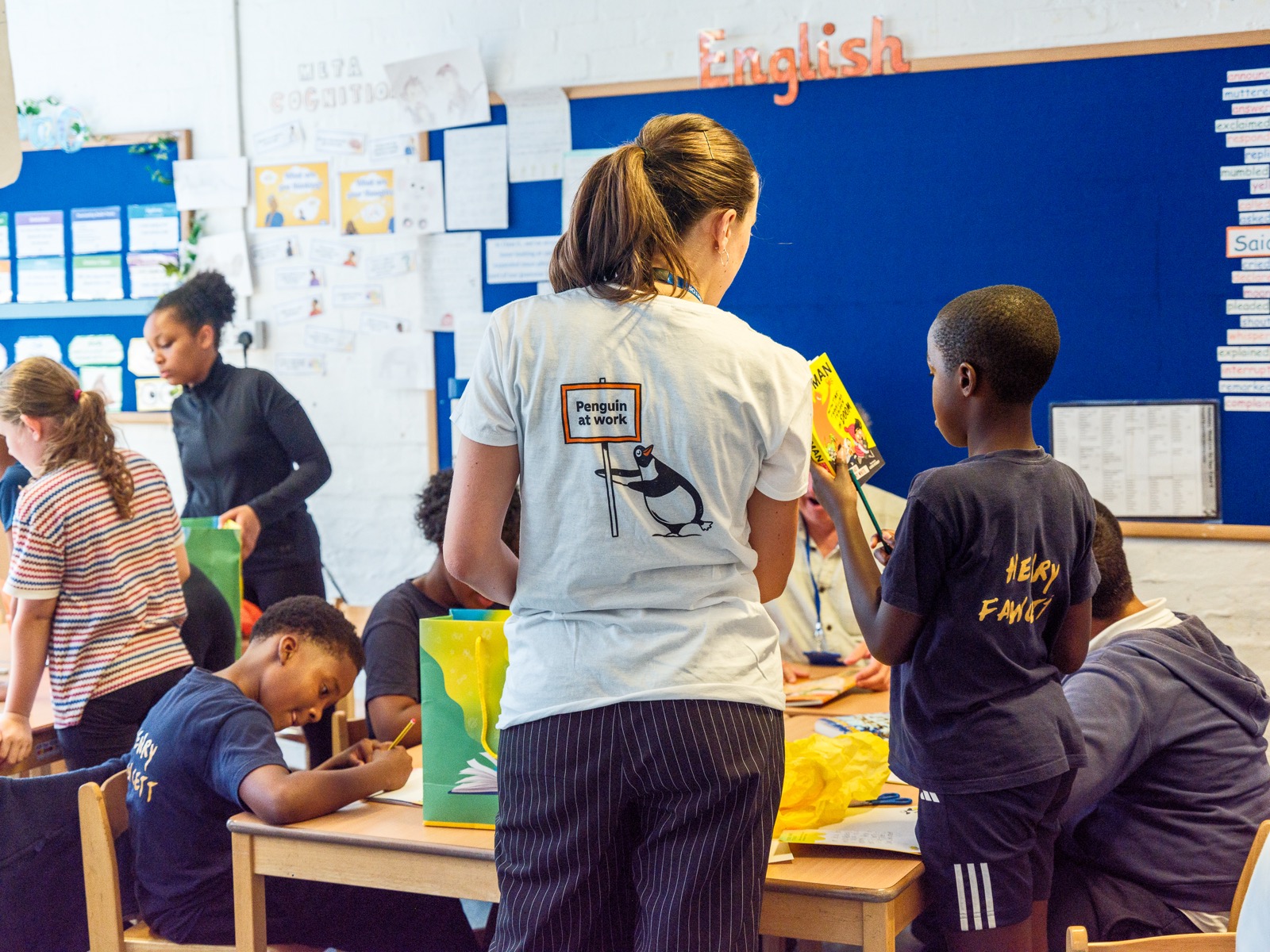 A Penguin volunteer in a "Penguin at work" T-shirt leading a reading and craft workshop with primary school pupils