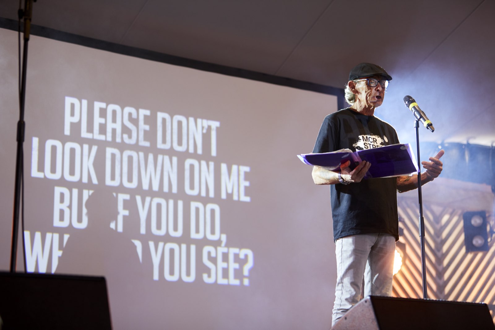 A spoken word performer on stage at Rise Like Lions, with projected text behind them