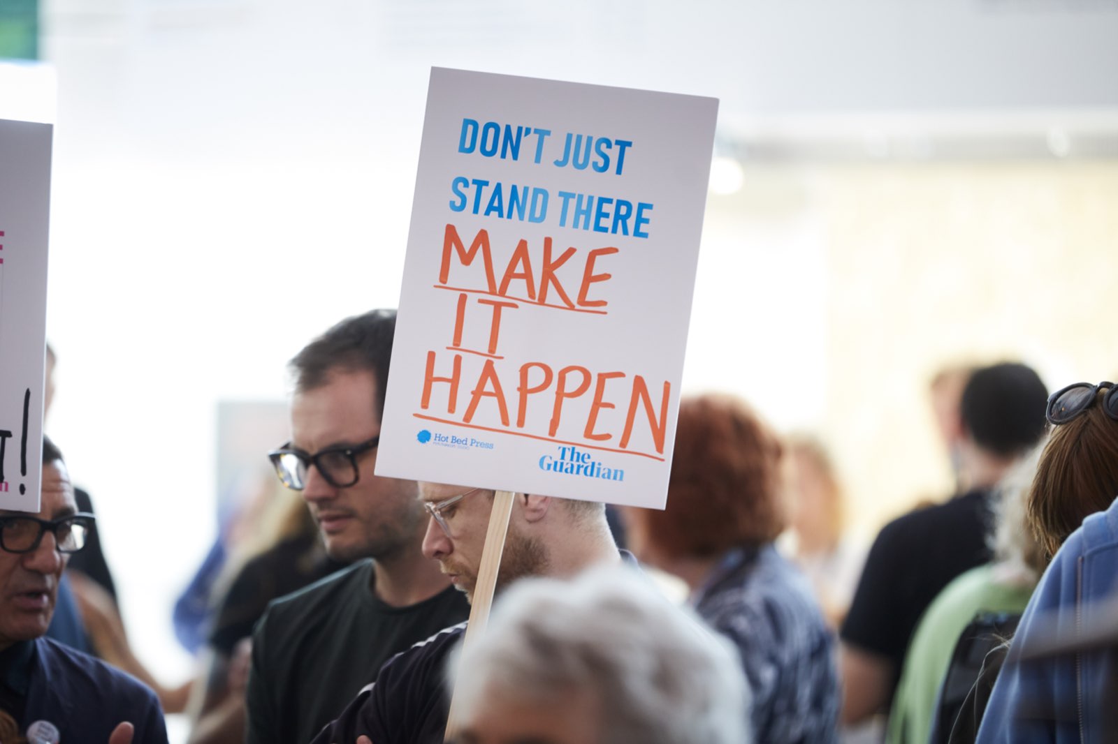 A Guardian placard reading Don't just stand there, make it happen held up in a crowd